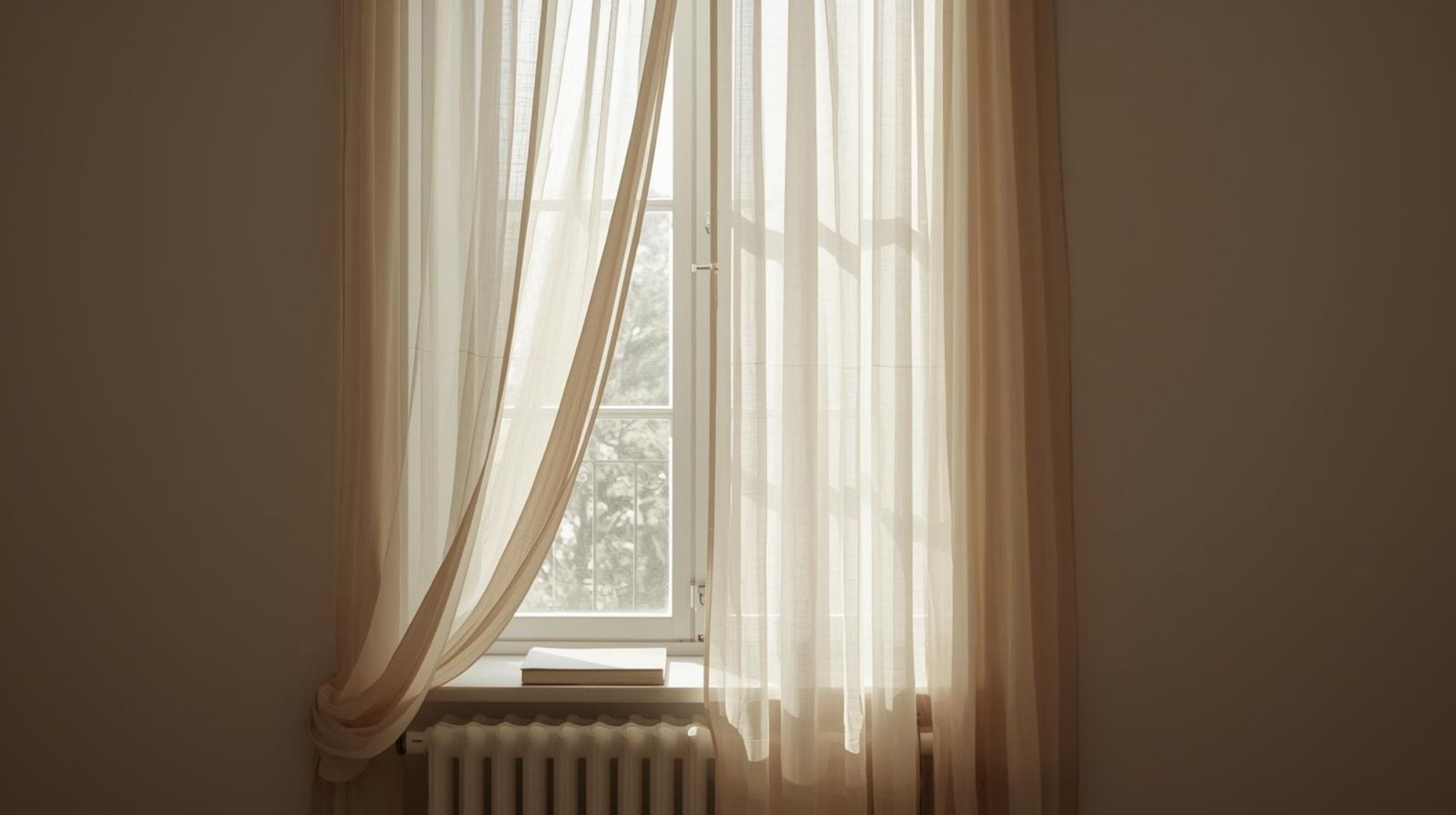 Sheer curtains hanging in front of a window with a book resting on the mantle